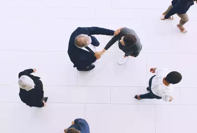 Aerial view of two people shaking hands while people walk by.