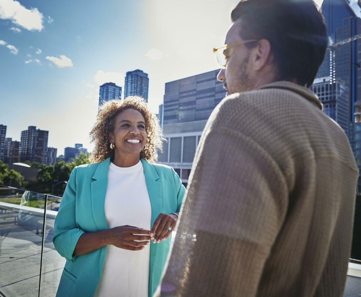 Female and male with glasses, standing outside on a balcony, talking