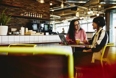 Two woman sitting in restaurant having a converstation, looking at laptop, smiling. Two woman sitting in restaurant having a converstation, looking at laptop, smiling.